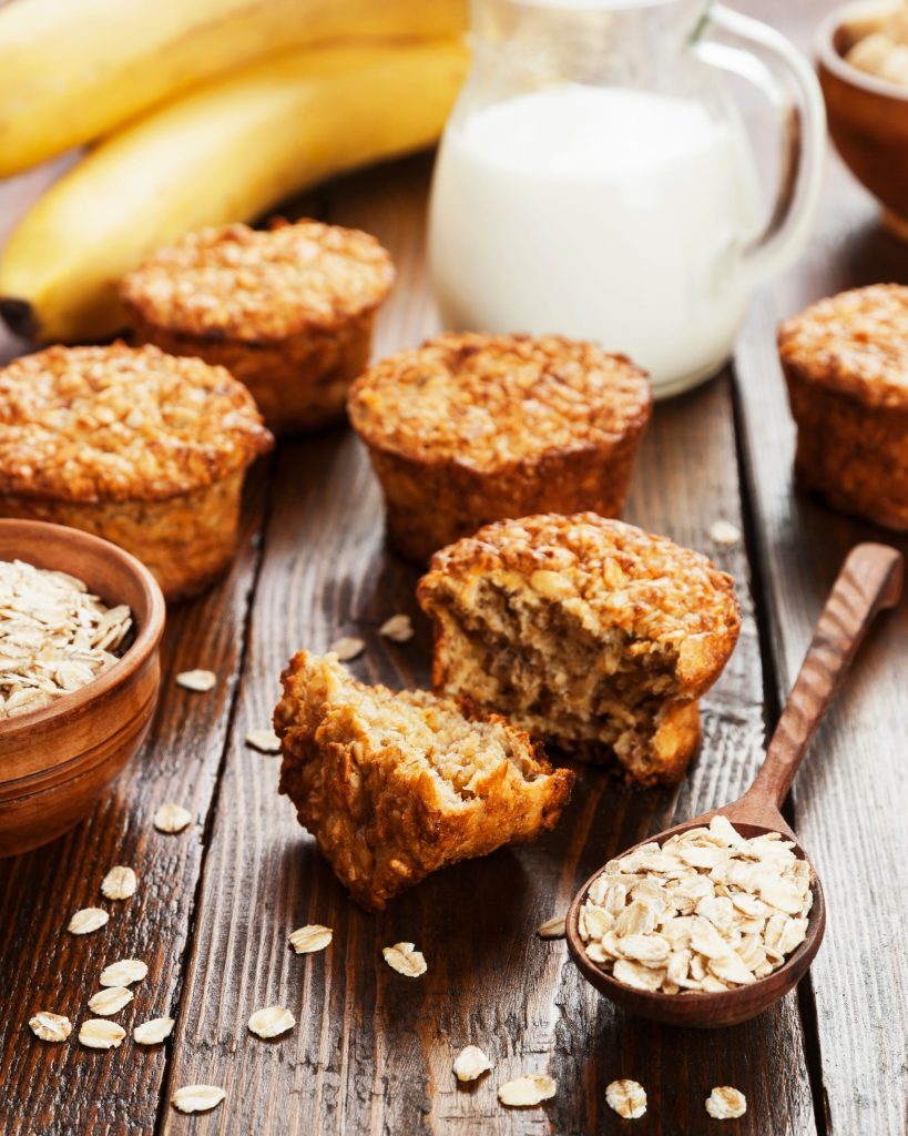 close up of banana oat muffins on wooden table with milk and oats