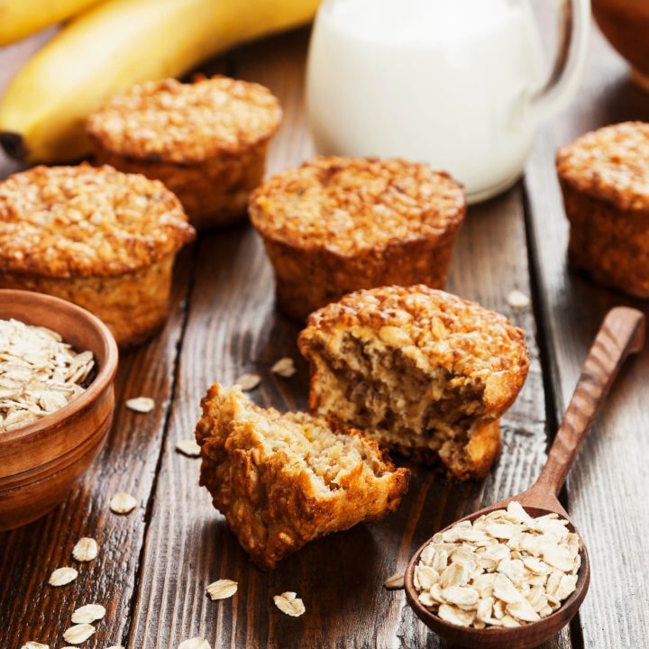 banana oat muffins on a wooden table with milk, oats, and bananas