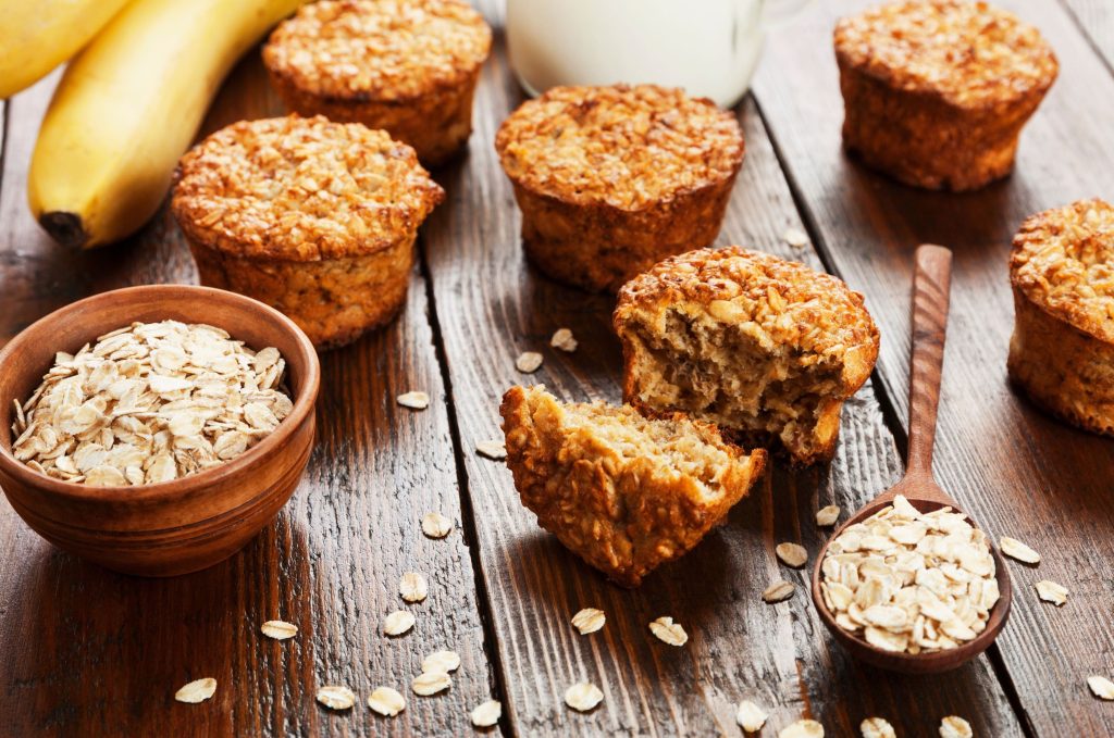 baked banana oat muffins on wooden table with bananas and oats