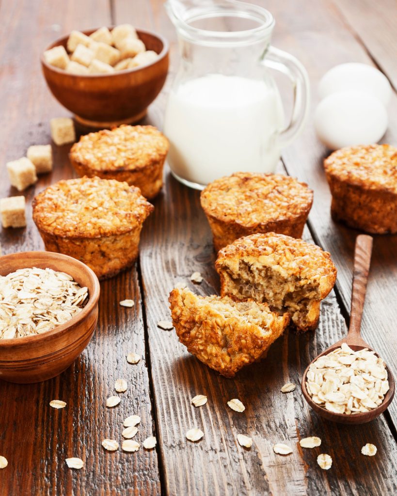 cooked banana oat muffins on a wooden table with milk, eggs, and oats