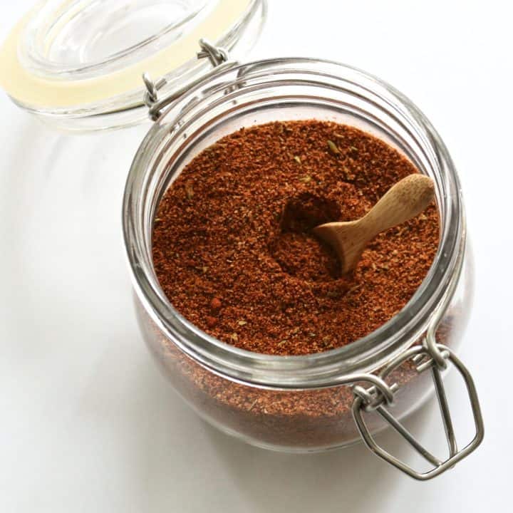 An image of homemade taco and chili seasoning mix in a glass jar with a wooden spoon.