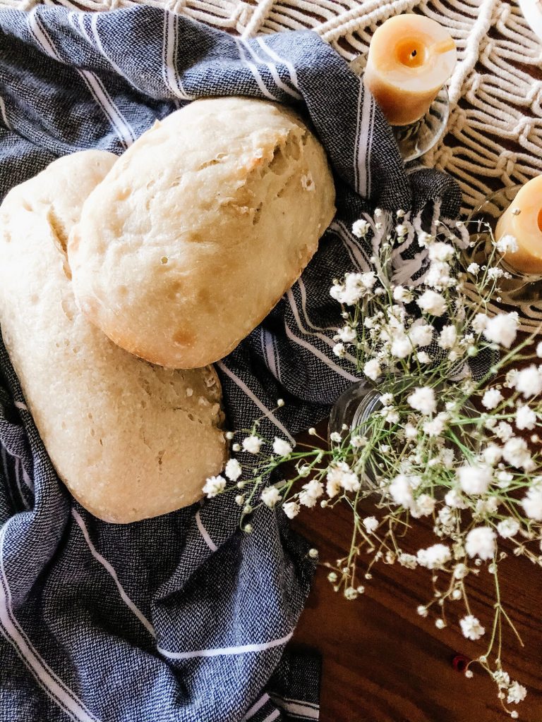 homemade overnight bread on a wooden table with beeswax candles and white flowers