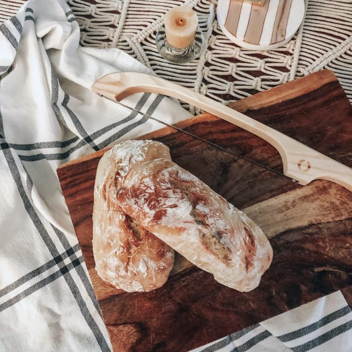 homemade bread on a wooden cutting board with bread bow and tea towel