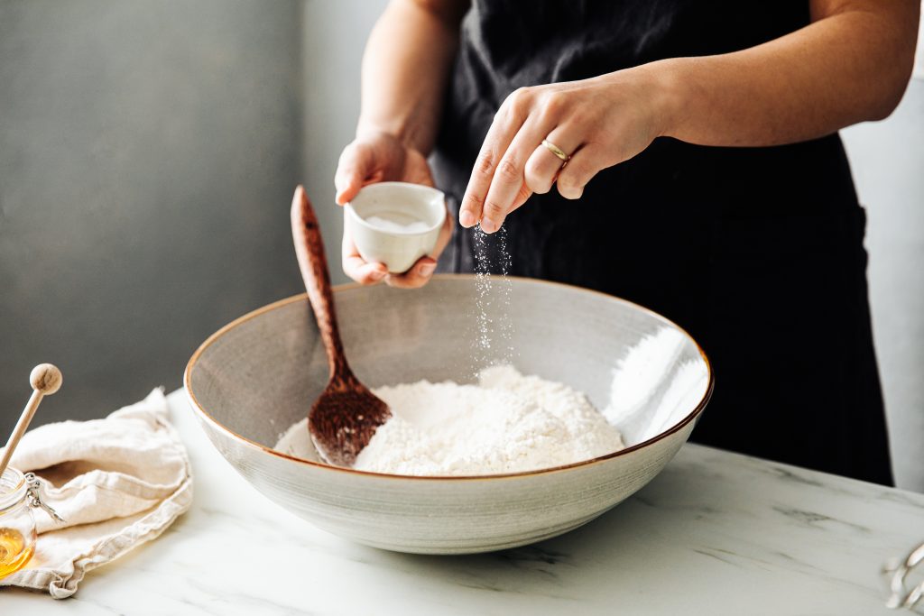 woman sprinkling salt in flour before mixing. 