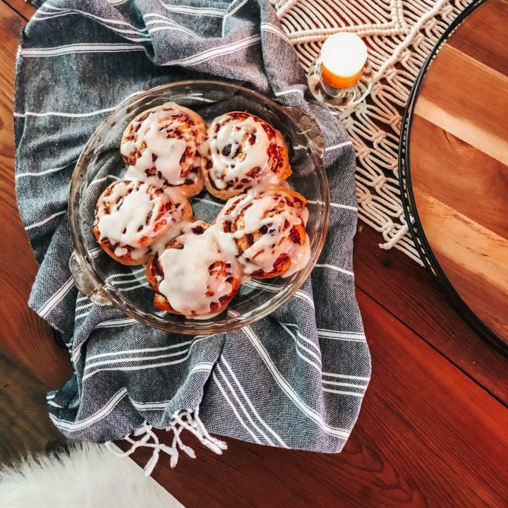 close up of iced cinnamon rolls in a dish on top of a black eta towel