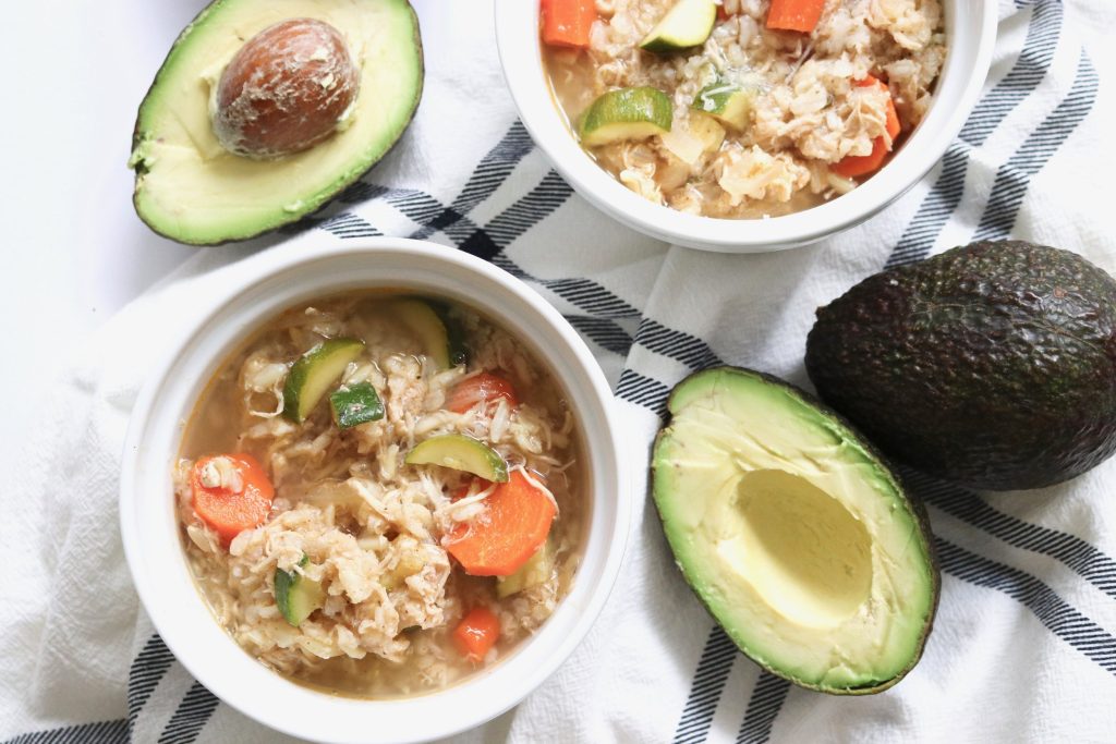 An image of two bowls of chicken tortilla soup next to a whole avocado and two avocado halves.