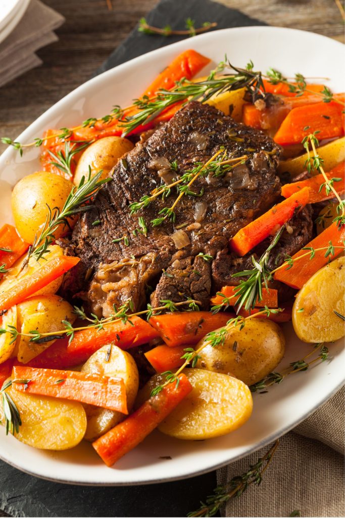 slow cooker roast on a white platter with fresh herbs, carrots, and potatoes