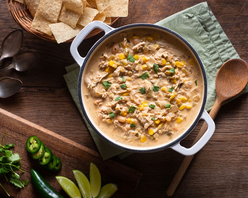 white chili on a green cloth on a wooden table with chips and peppers