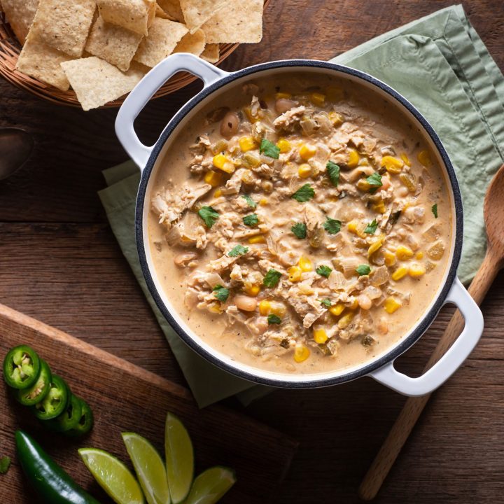 white bean chili in a large pot on a wooden table with chips, limes, and peppers