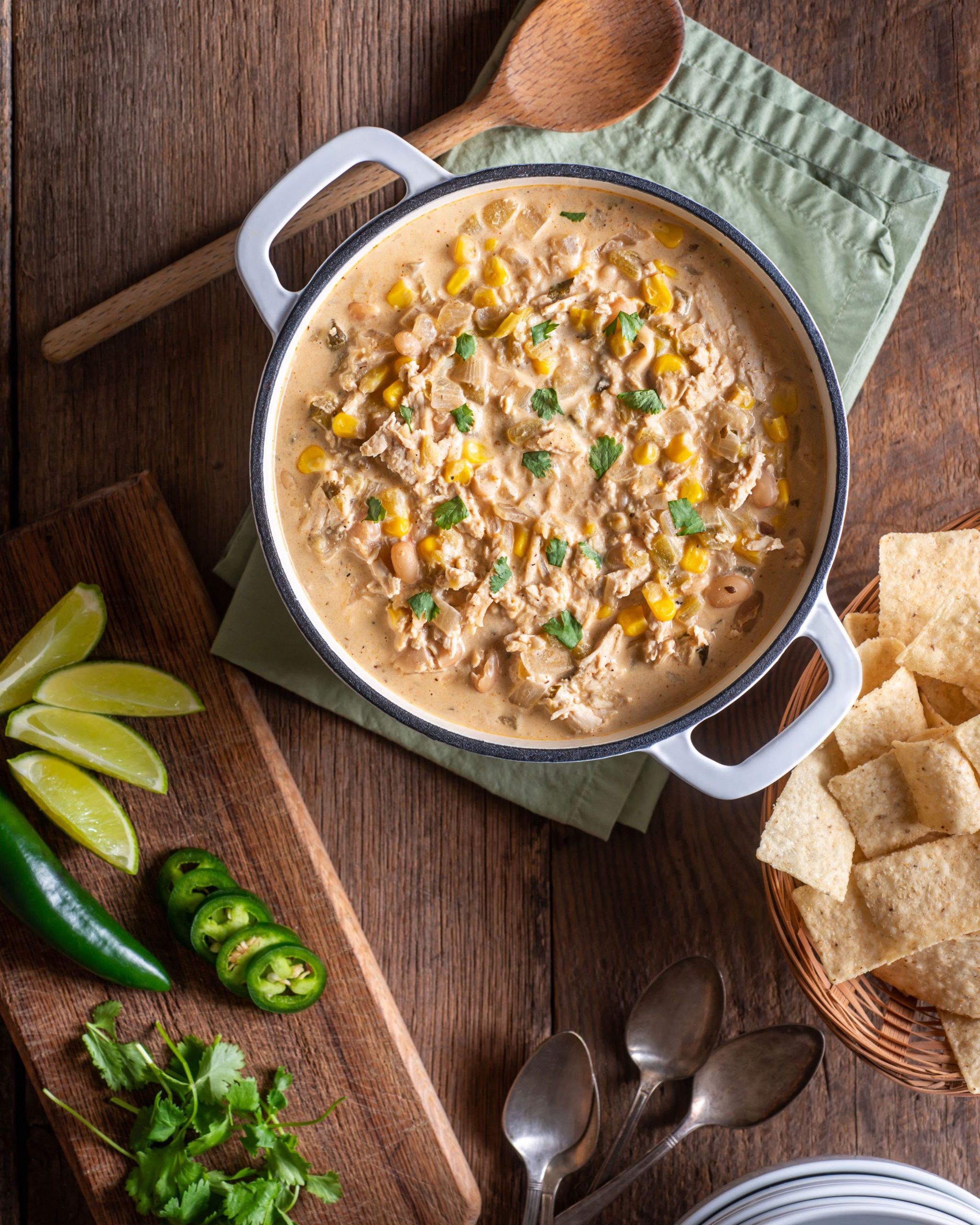 pot of white chili on wooden table with limes, chips, and peppers