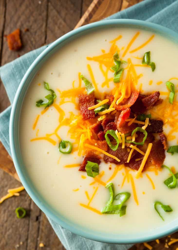 Close up of loaded potato soup with cheese, bacon and green onions on a wooden table