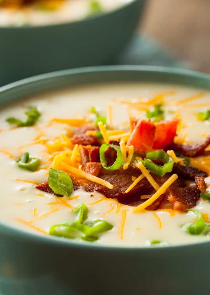 Close up of potato soup with cheese, bacon and green onions on a wooden table