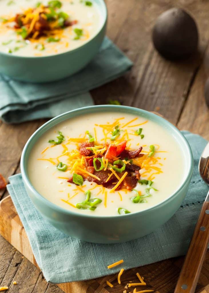 Two bowls of potato soup with cheese, bacon and green onions on a wooden table