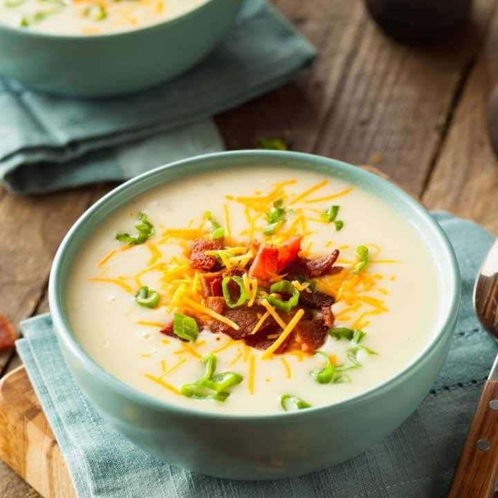 Close up of potato soup with cheese, bacon and green onions on a wooden table