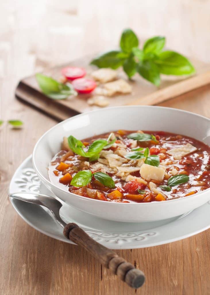 Minnestrone soup garnished with basil in a while bowl on a wooden table