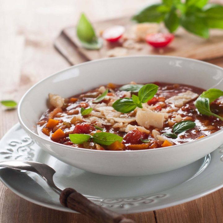 Minnestrone soup garnished with basil in a while bowl on a wooden table