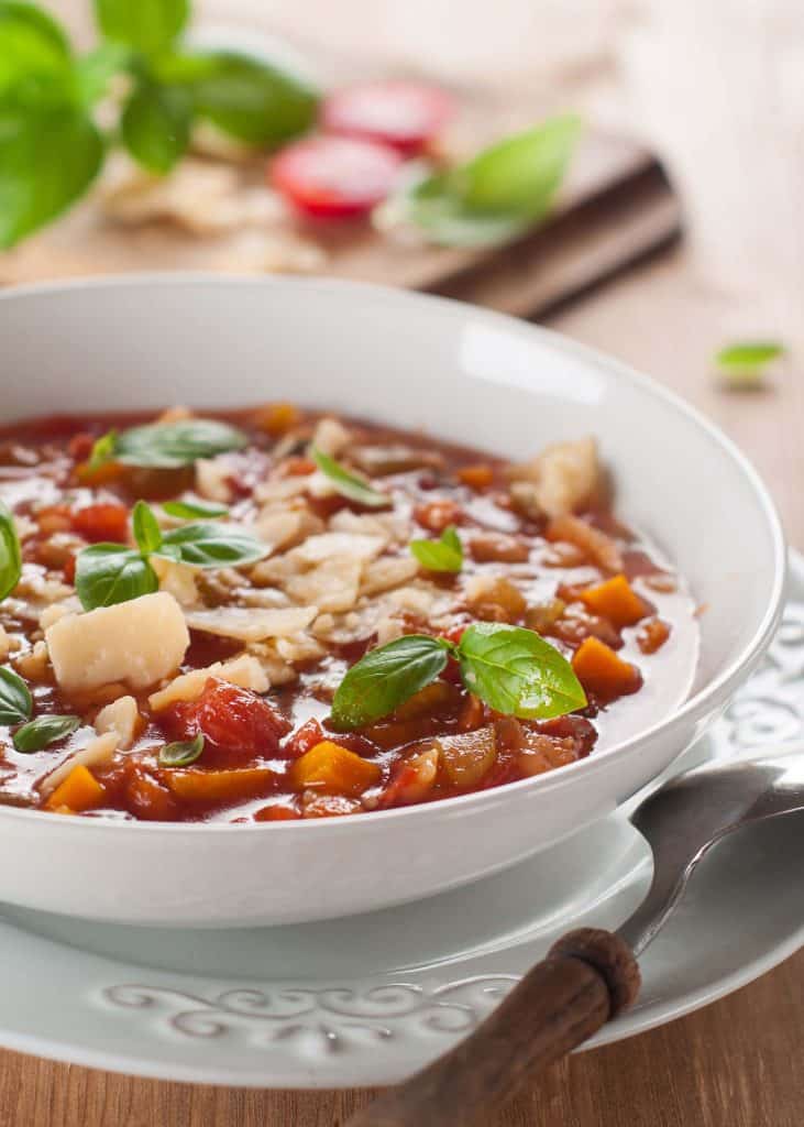 Minestrone soup garnished with basil and parmesan in a while bowl on a wooden table