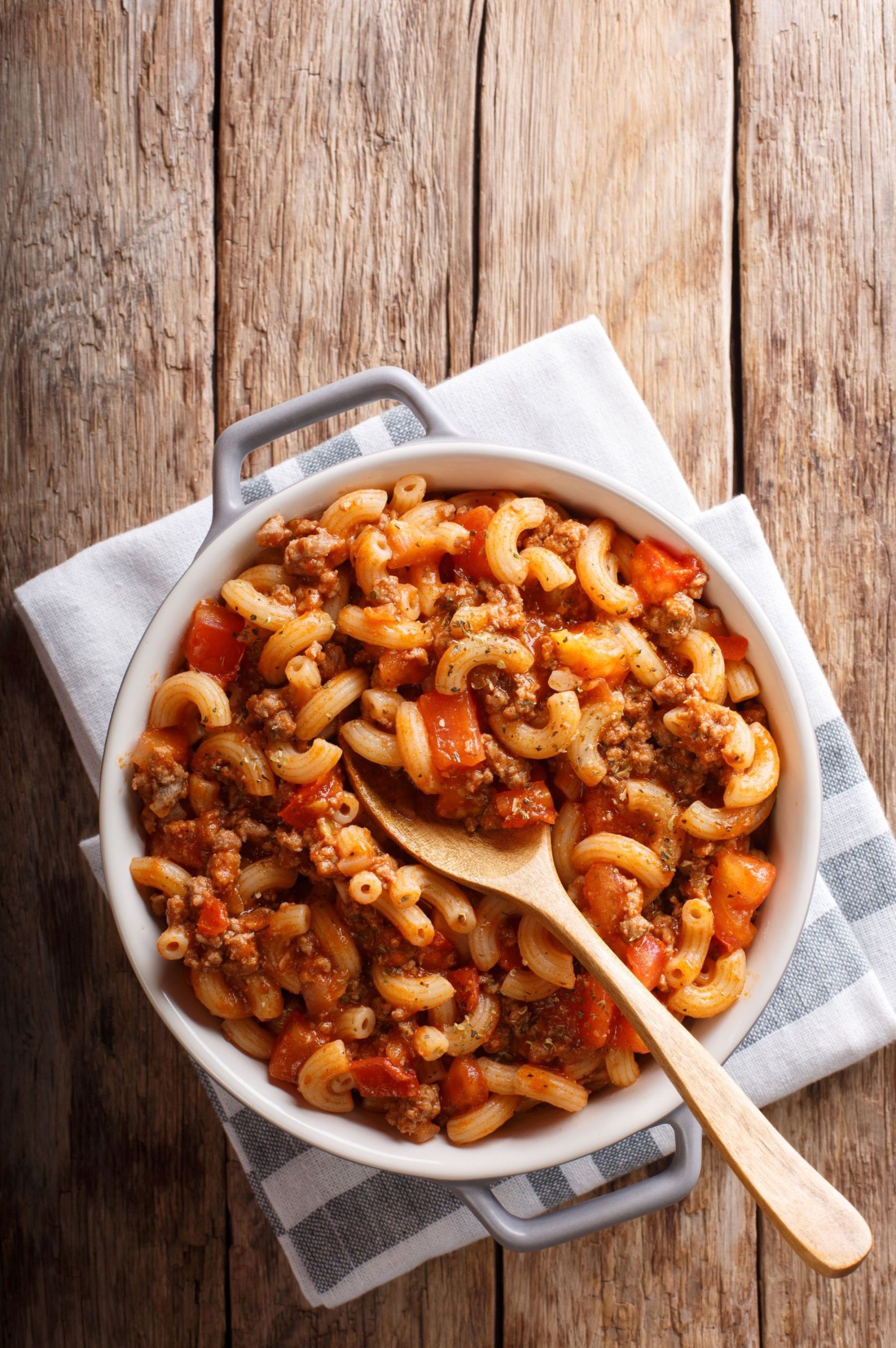 pasta, tomatoes, and meat in a bowl with wooden spoon