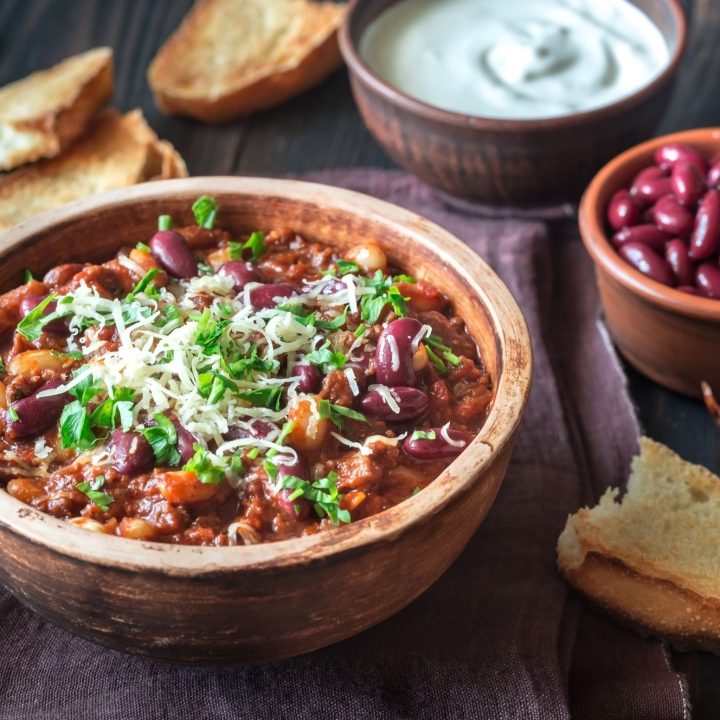 close up of chili in a wooden bowl with cheese and cilantro