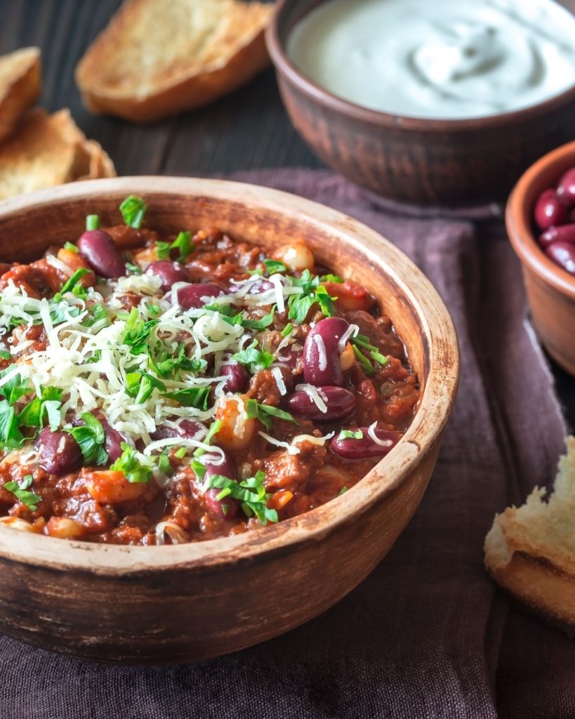 Close up of chili in a wooden bowl with sour cream and beans behind it