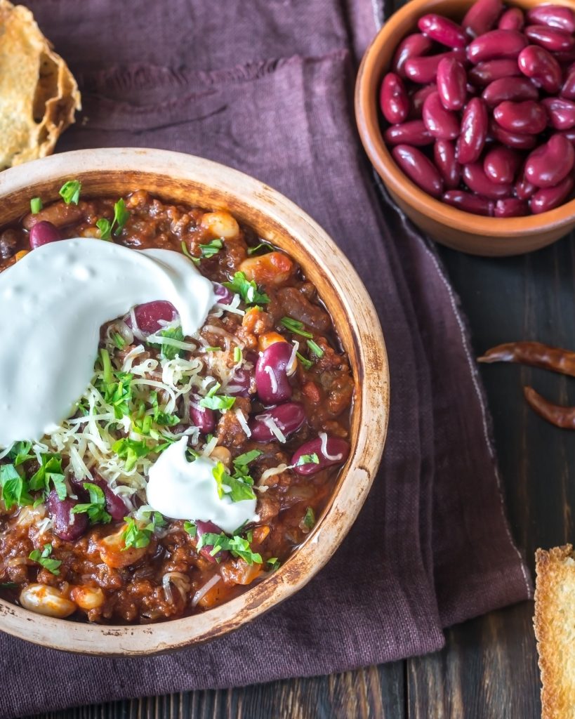 close up of chili in a wooden bowl with sour cream and beans