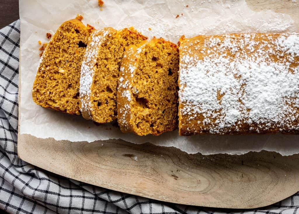 Close up of sliced pumpkin bread on parchment, topped with dusted powdered sugar.