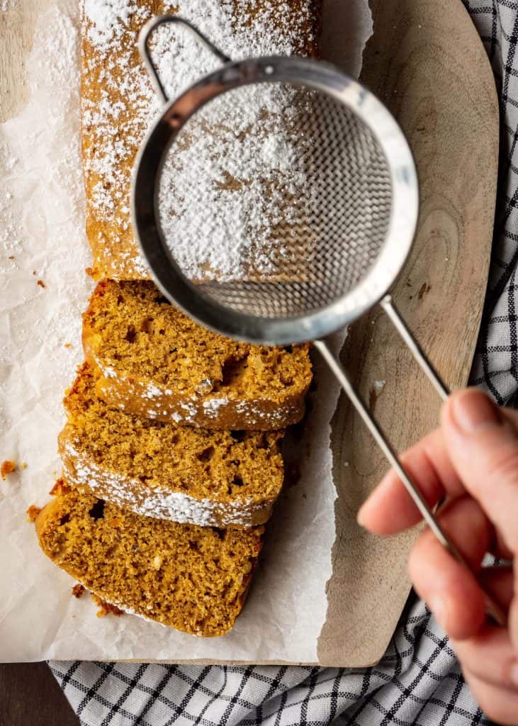 and sifting powdered sugar onto loaf of pumpkin bread