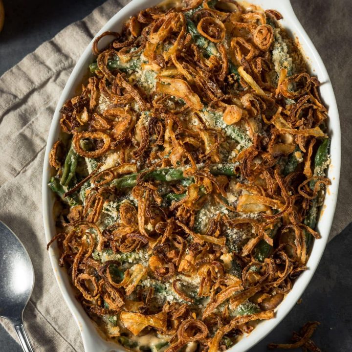 Delicious, healthy green bean casserole in a white oval baking dish topped with crispy onions and sitting atop a beige dish towel.