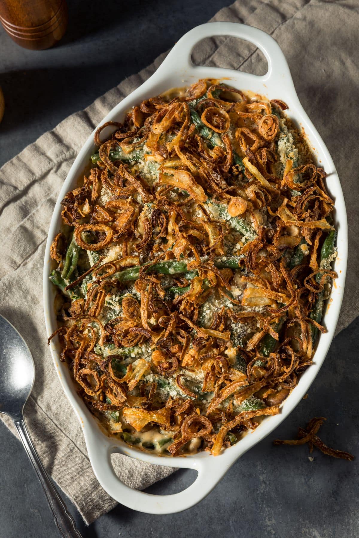 Delicious, healthy green bean casserole in a white oval baking dish topped with crispy onions and sitting atop a beige dish towel.