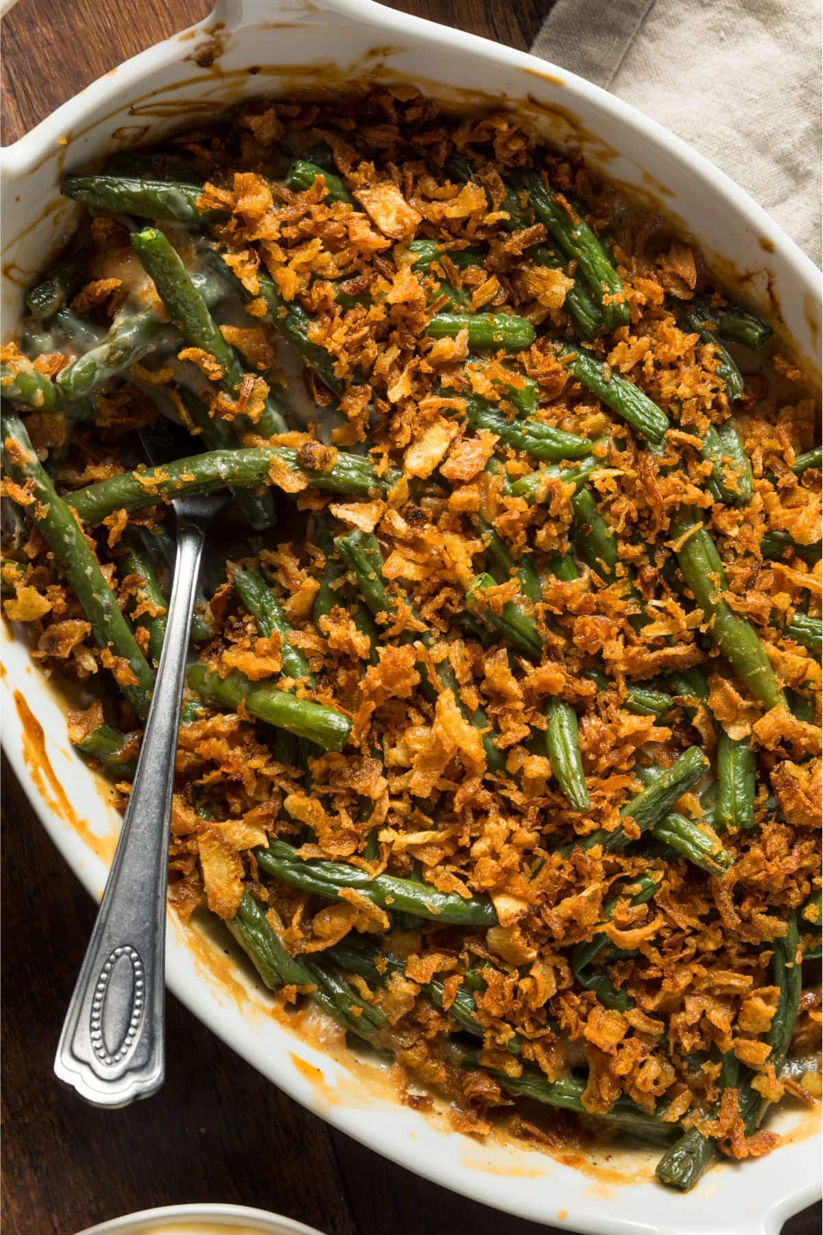 Close up of green bean casserole in a white ceramic baking dish topped with homemade onion crisps