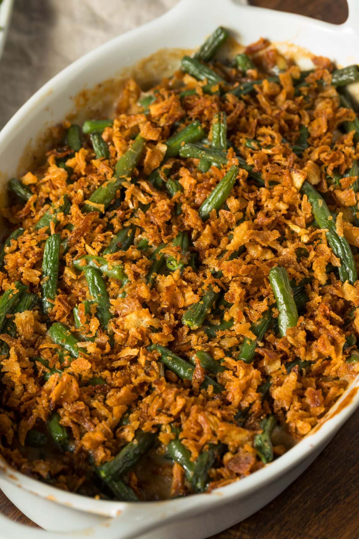 Close up of a delicious, homemade green bean casserole in a white dish topped with crispy onions.