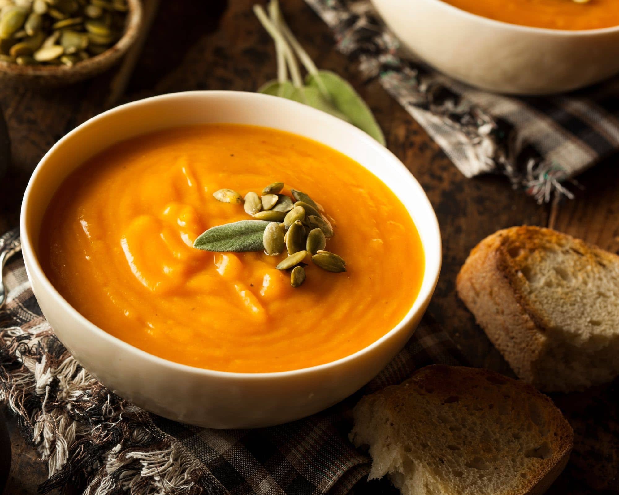 Bowls of creamy butternut squash carrot soup beside crusty bread on a wooden cutting board.