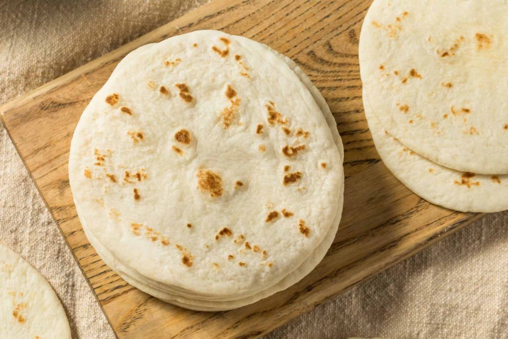 two piles of soft sourdough tortillas upon a wooden cutting board, ready to be turned into something delicious!