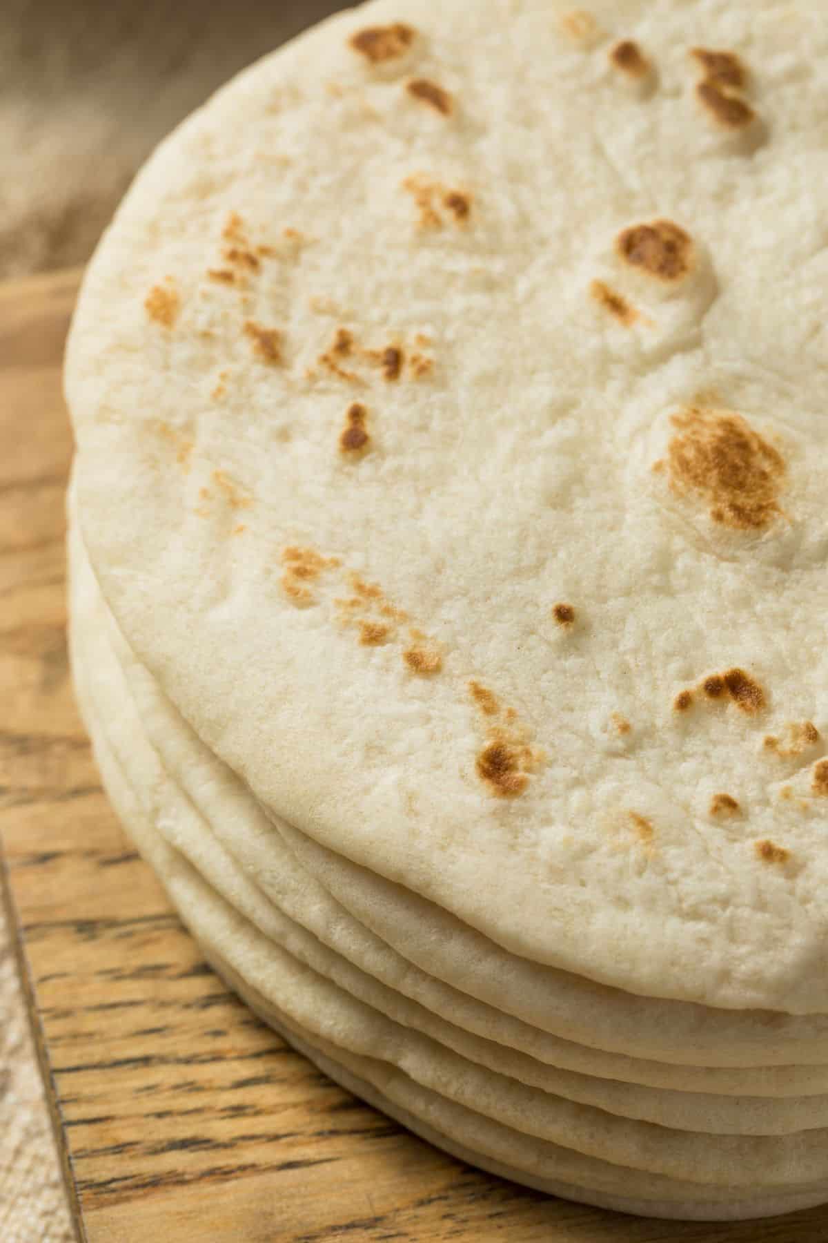 close up of soft sourdough tortillas stacked upon a wooden cutting board, ready to be turned into something delicious!