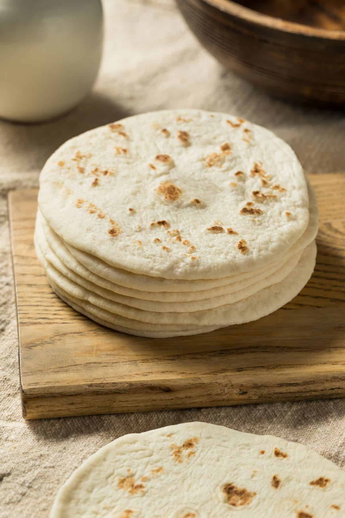 soft sourdough tortillas stacked upon a wooden cutting board, ready to be turned into something delicious!