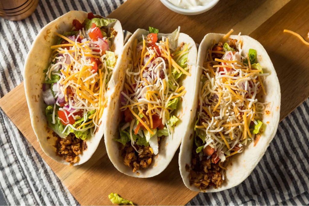 sourdough tortillas filled with delicious taco ingredients--ground meat, lettuce, onions, tomatoes, and topped with cheese--sitting on a cutting board.