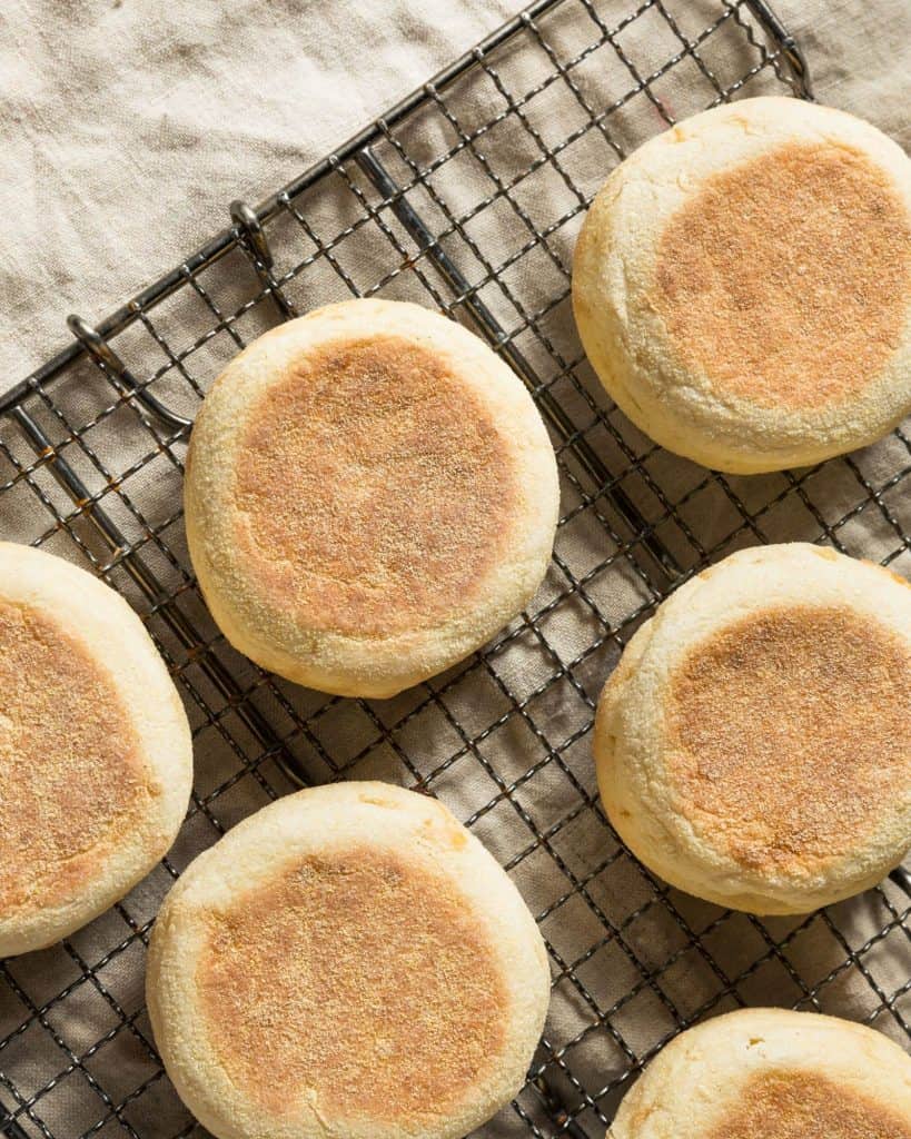 Fresh sourdough English muffins on a cooling rack with a beige towel.