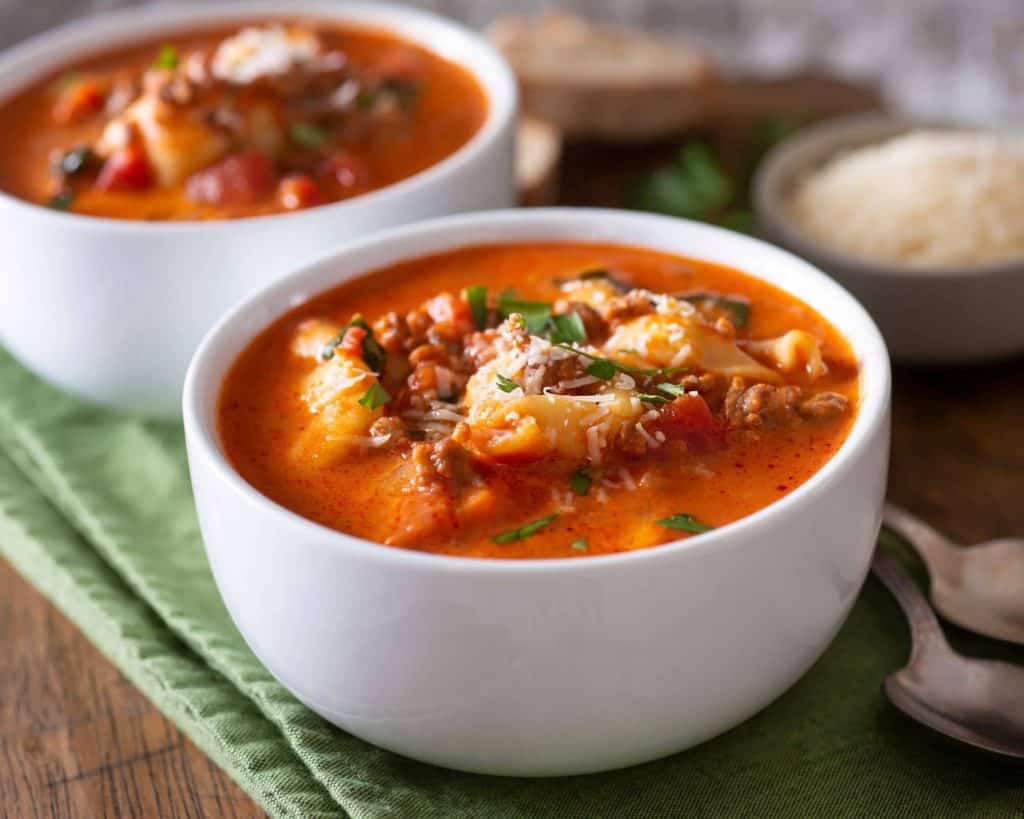 Two bowls of delicious, hearty tortellini soup with kale and ground beef on a cutting board and green napkin.