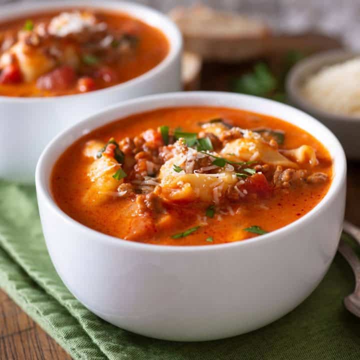 Two bowls of delicious, hearty tortellini soup with kale and ground beef on a cutting board and green napkin.