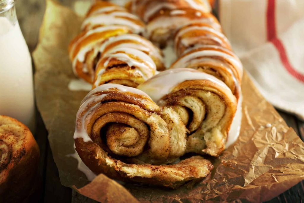 Close up of a loaf of iced cinnamon pull-apart bread, warm and fresh from the oven, with a glass of milk waiting to be shared!