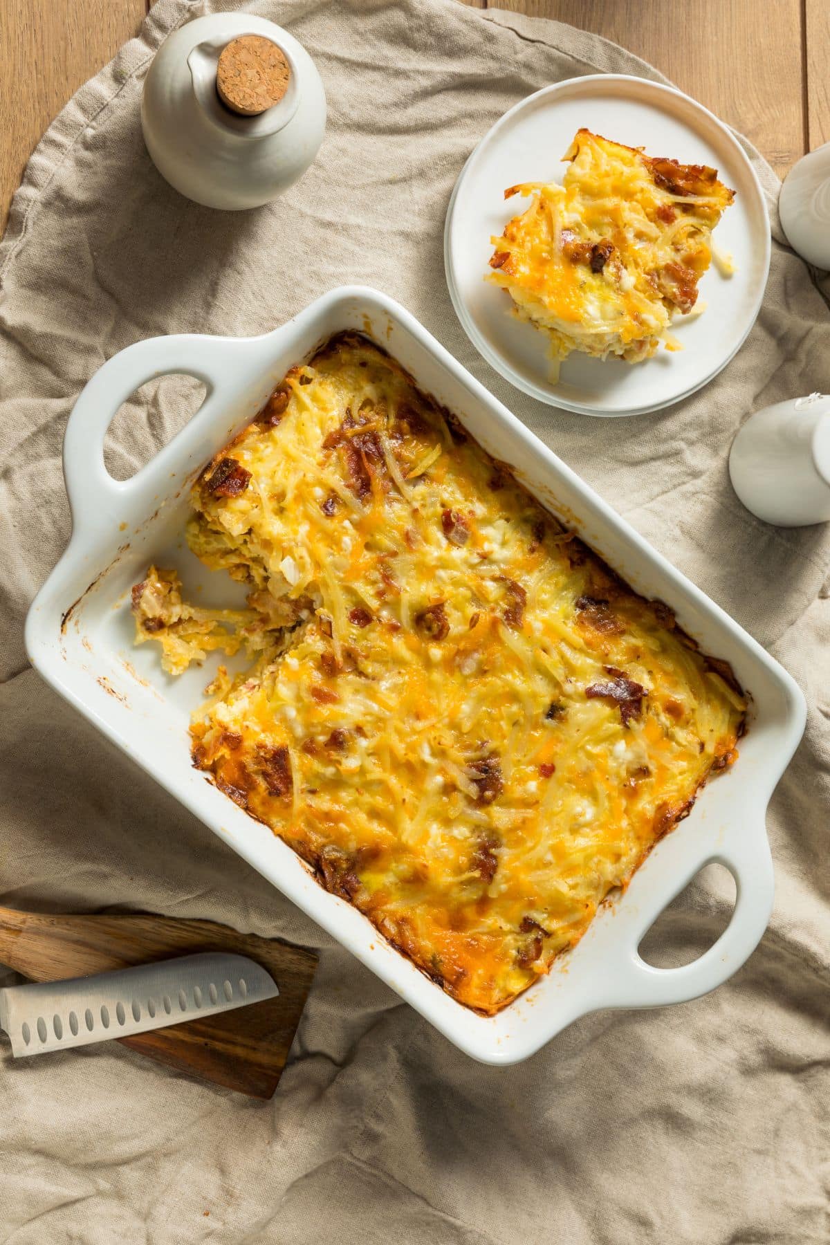 Cheesy breakfast casserole with eggs and protein in a white baking dish beside a plate of the casserole waiting to be dug into!