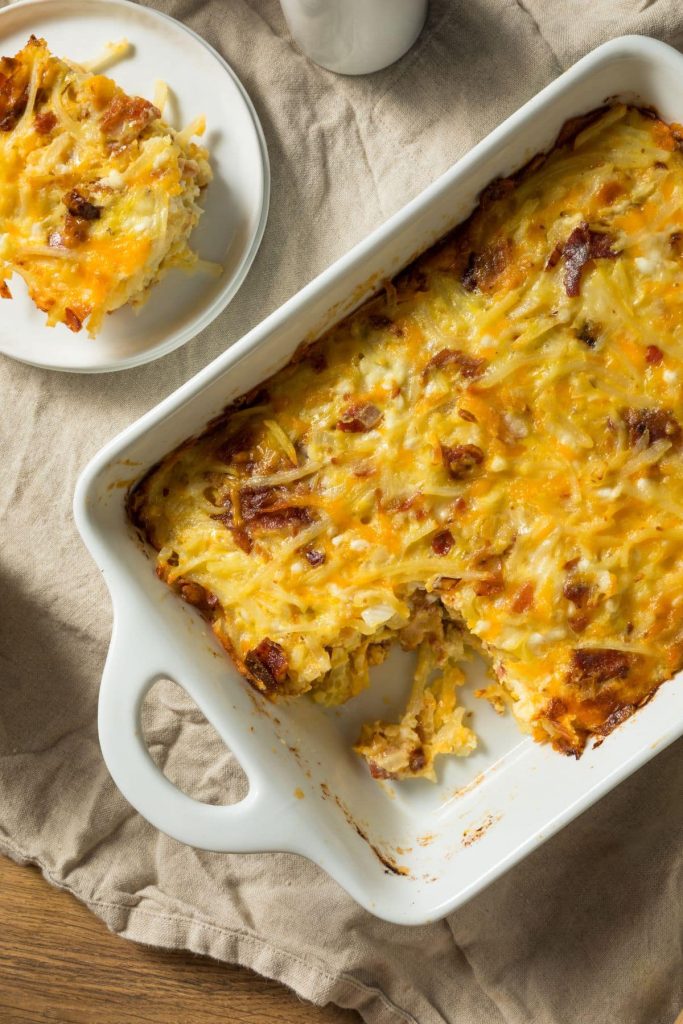 Cheesy breakfast casserole in a white baking dish with a plate of the casserole waiting to be eaten. 