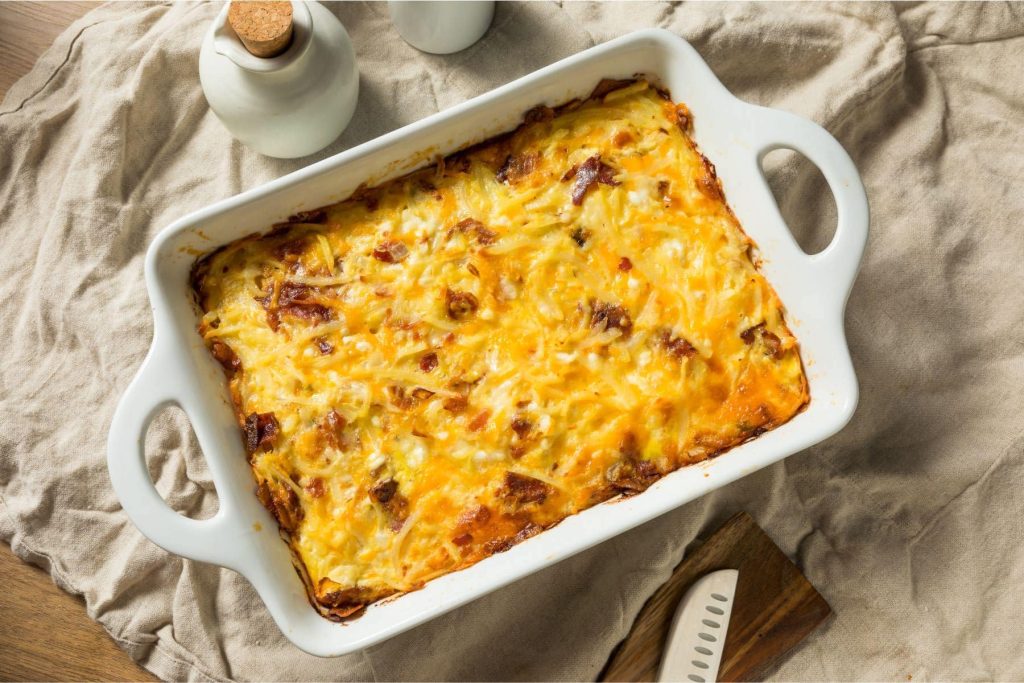 Delicious, protein-packed breakfast casserole on a tan tablecloth in a white baking dish.