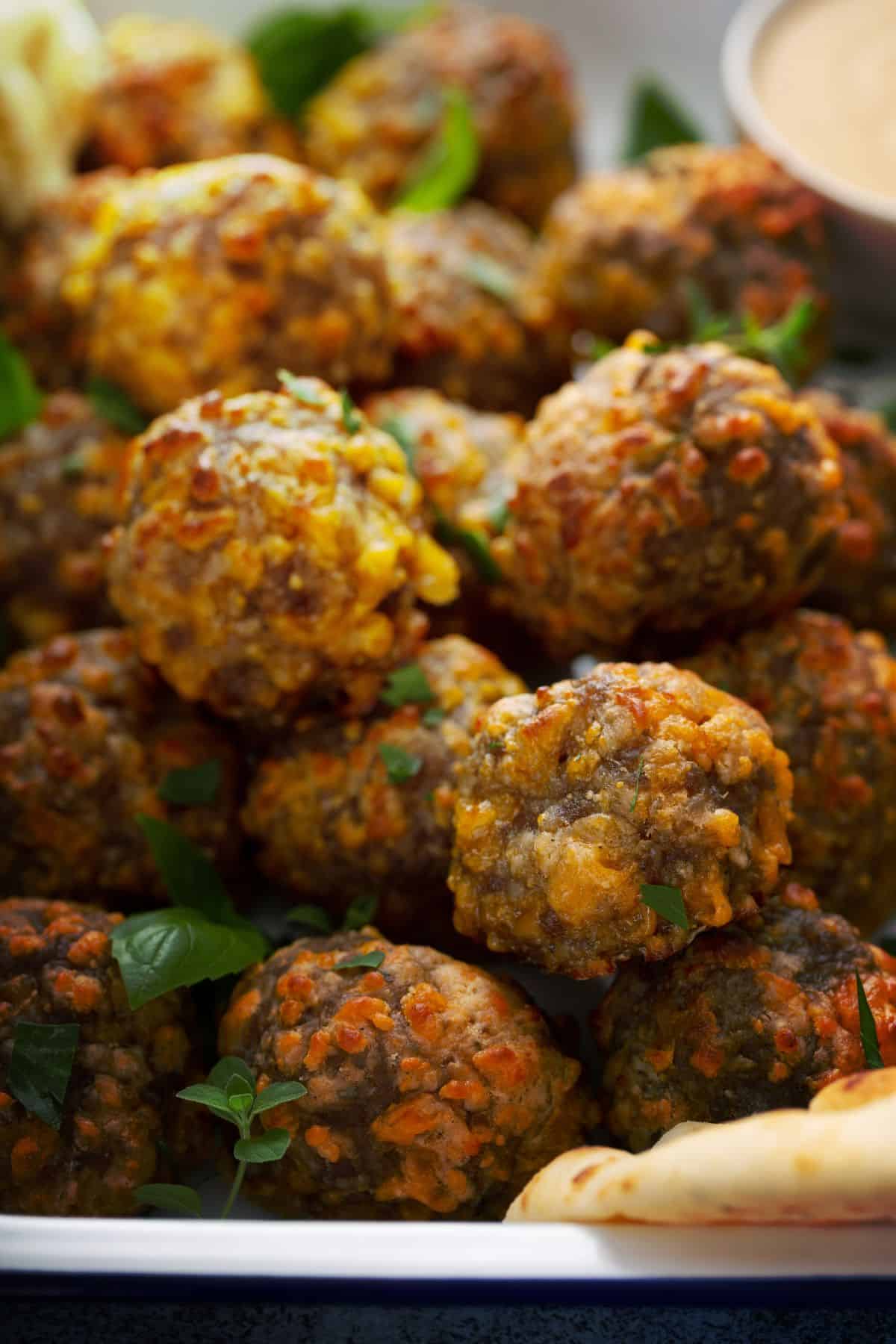 Close up of golden, crispy sausage balls in a white baking tray with dipping sauce and in the background.