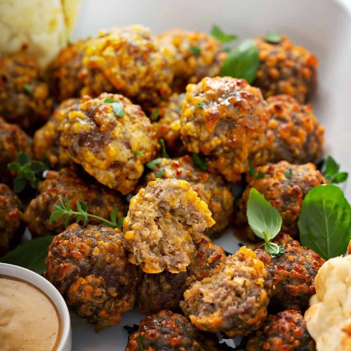 Close up of golden, delicious sausage balls in a white tray with dipping sauce and fresh pita