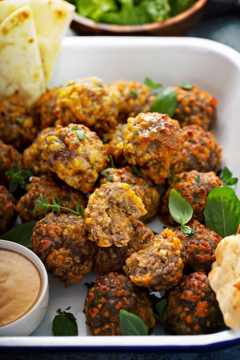 Close up of golden, delicious sausage balls in a white tray with dipping sauce and fresh pita