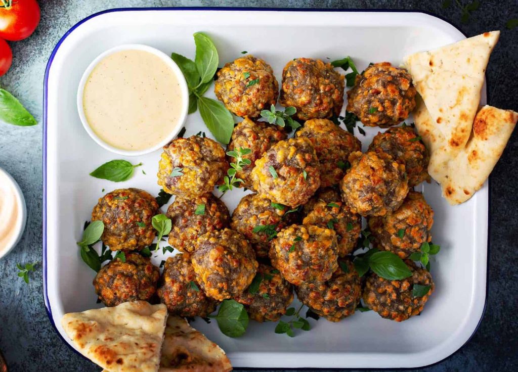 White tray full of golden, delicious sausage balls iwith a bowl of dipping sauce, fresh herbs, and fresh pita bread - the perfect appetizer!