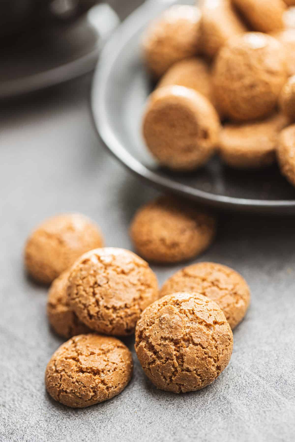 A fresh batch of soft almond sugar cookies on a grey counter with a bowl full of freshly baked cookies behind it.