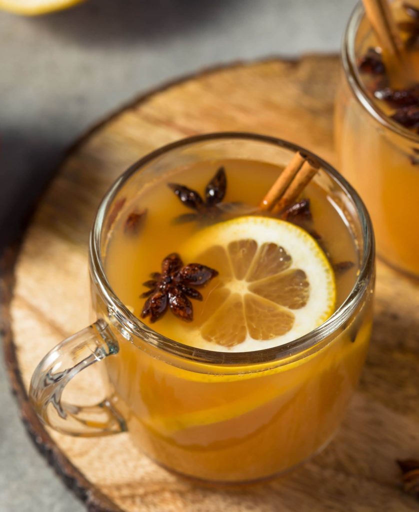 A mug of wassail topped with lemon slices, anise, and cinnamon sticks sitting on a wooden cutting board.