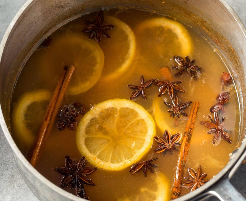 Close up of wassail in a simmer pot topped with lemon slices, anise, and cinnamon sticks.